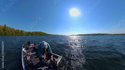 Angler in the boat during windy day and large waves removing trolling motor mounted to the bow for changing the fishing spot. Trolling motor electric propulsion system for slow movement while fishing.