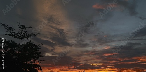 Dramatic sunset sky with orange and golden glow behind dark storm clouds