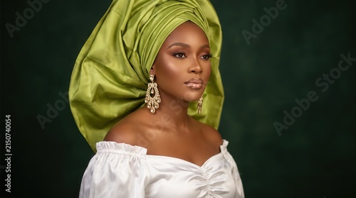Portrait of a beautiful african woman wearing a traditional green gele headwrap and elegant white offshoulder top