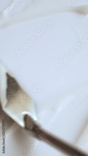Thick white cosmetic cream being smoothed with a metal spatula creating a textured background