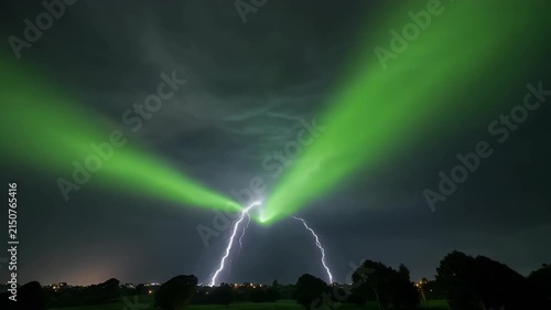 A dramatic green aurora borealis illuminates the night sky, intersecting with a powerful lightning strike above a silhouetted landscape.