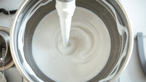 White viscous liquid swirling in an industrial mixer bowl, gradually thickening its consistency.