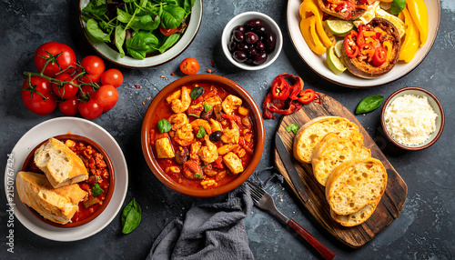 Spanish tapas food flat lay banner with Mediterranean dishes, seafood stew, bruschetta, tomatoes, and olives on a dark background