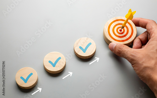 Hand placing a wooden target block with yellow dart next to completed checkmark progress steps