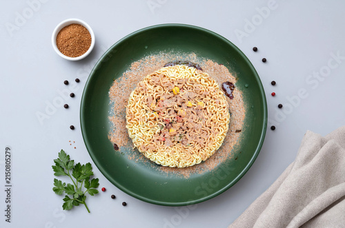 Instant ramen noodles with seasoning on green plate, overhead flat lay on gray background
