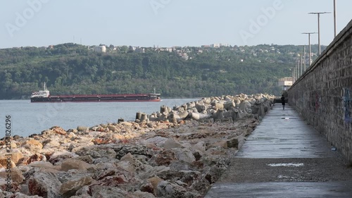 Cargo ship sailing past a breakwater with person walking