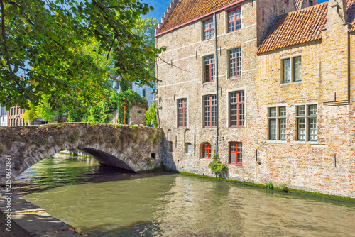 Bruges town in Belgium, Europe. Historic Stone Bridge Traverse Calm Canal Waters, Flanked by Traditional Brick Buildings on a Bright Sunny Day, Old Town Architecture