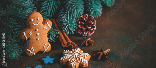 Gingerbread man on dark grunge background with Christmas decorations, fir branches, spices, stars, selective focus, copy space.
