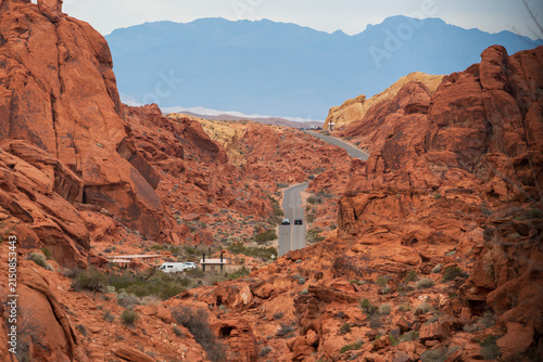 Desert highway runs between red sandstone cliffs and distant mountains in Valley of Fire State Park, Nevada.
