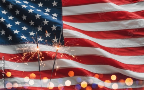 Sparkling firework sparklers glowing brightly in front of a waving american flag background, celebrating independence day with patriotic spirit and festive holiday lights
