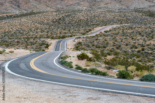 Lonely asphalt road winds across open Mojave desert terrain near Valley of Fire State Park, Nevada.