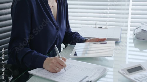 Professional woman using digital tablet for business tasks, typing data and reviewing documents at a modern office desk, symbolizing efficiency and financial management