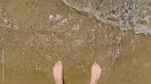 Close first person view of ocean waves flowing over bare feet on golden sand capturing a peaceful summer vacation moment by the sea. High quality FullHD footage