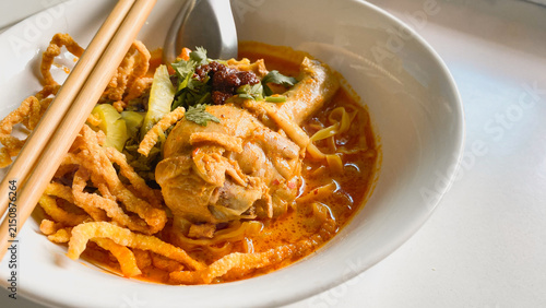 Traditional Northern Thai chicken khao soi curry noodle soup served with tender chicken, crispy noodles, pickled mustard greens, fresh herbs, and rich aromatic coconut curry broth in a white bowl.