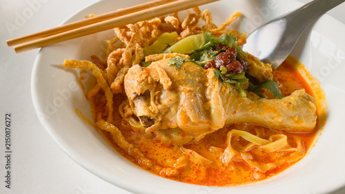 Traditional Northern Thai chicken khao soi curry noodle soup served with tender chicken, crispy noodles, pickled mustard greens, fresh herbs, and rich aromatic coconut curry broth in a white bowl.