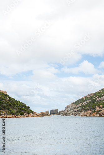 Konstfotografi Vertical coastal scene at Wychinicup Inlet showing calm water between rocky, vegetation-covered hills under a partly cloudy sky
