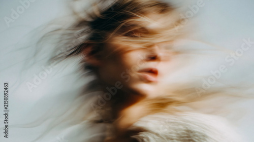 Female face disappears into soft motion blur during a quiet moment in daylight as hair flows across her skin to create a minimalist scene of movement and grace