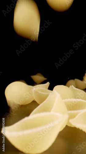MACRO: Uncooked conchiglie pasta fall on a black table, Slow motion