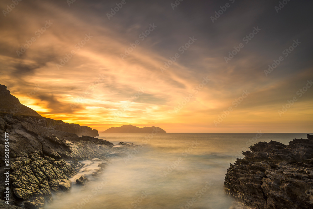 Obraz premium Dramatic sunset sky over rocky coast with long exposure flowing sea waves in Sonabia Cantabria Spain
