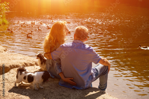Fotografía Mature Couple with Dogs by a Pond in Warm Evening Light