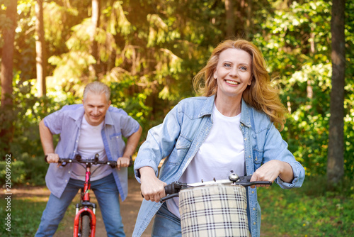 Fotografía Smiling Mature Woman Cycling on a Green Forest Path