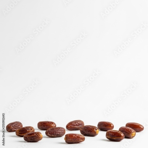 A group of whole dried brown dates scattered across the bottom of a white background with a large amount of empty white space above for copy and design placement.