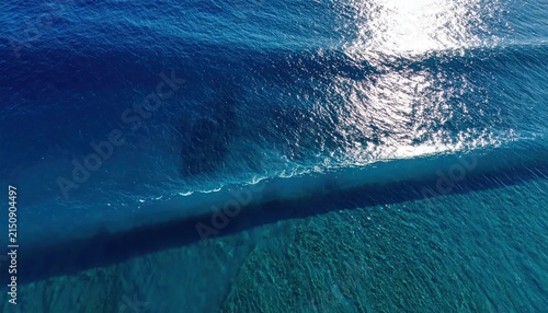 Aerial view of a clear blue ocean wave breaking.