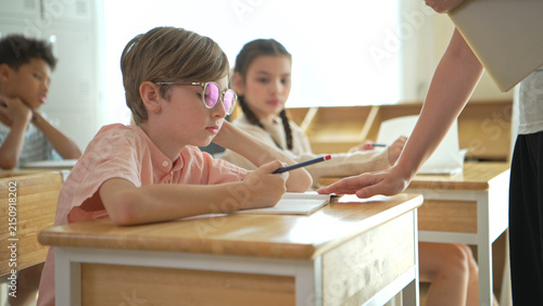 Photography Schoolboy looking bored and distracted in classroom while classmates study,