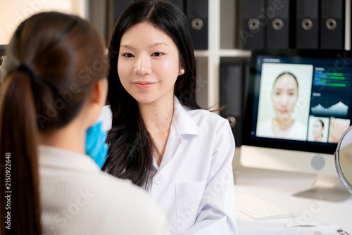 Young asian woman doctor examining face of woman patient in aesthetic clinic during computer screen display AI software for skin scanning and analysis result, evaluating and diagnostic skin facial.