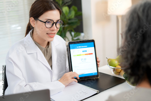 Asian woman nutritionist showing AI BMI calculator on tablet and explaining to senior patient, doctor using digital health technology for medical diagnosis, wellness planning and weight control.