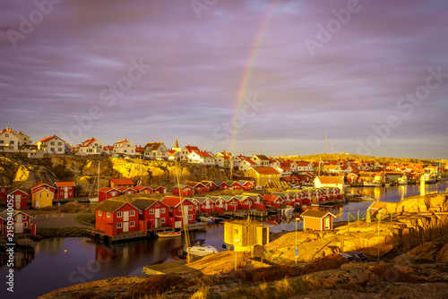 Smögen harbor and red wooden boathouses under a rainbow at sunset, Sweden