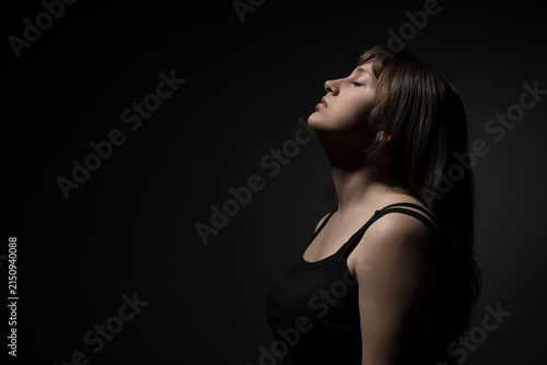 Young woman with closed eyes feeling peaceful in dark studio