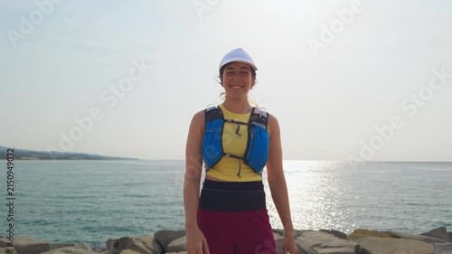 Person stands on rocky shore wearing a life vest and helmet. The ocean stretches behind them in calm waters. She smiles as another hand reaches out for a high-five. This joyful moment suits adventure