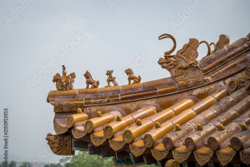 Ornate golden glazed roof tiles and mythical guardian figurines line the curved eaves of a traditional Chinese imperial temple under a grey, hazy sky.