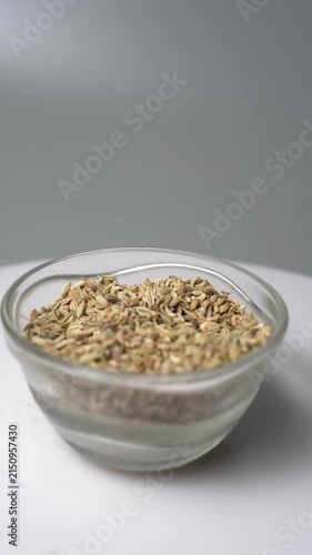 A close-up shot of a hand gently pouring dried fennel seeds into a glass bowl, showcasing the aromatic spice ready for cooking or traditional remedies