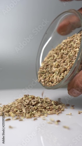 Close-up of Fennel Seeds Pouring from a Glass Bowl onto a White Surface for Cooking and Health Applications