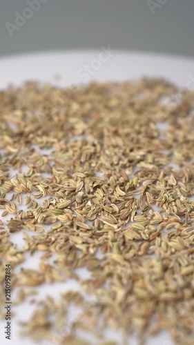 A close-up view of whole fennel seeds on a white surface, slowly rotating to showcase their texture and natural color