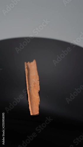 Close-up of a Cinnamon Stick Slowly Rotate on a Black Reflective Surface, Capturing the Rustic Texture and Warm Brown Tones of the Spice