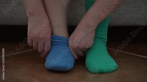 Close-up of woman's hands putting on mismatched socks of different color on her feet. Woman wearing different colored socks. Uniqueness, difference and independence concept. Front view