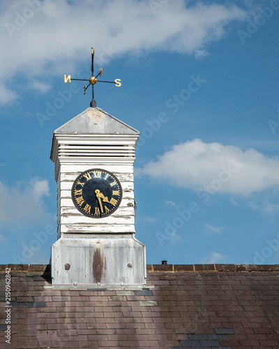 Weathered English clock tower and weathervane against blue sky with generous copy space for vertical design.