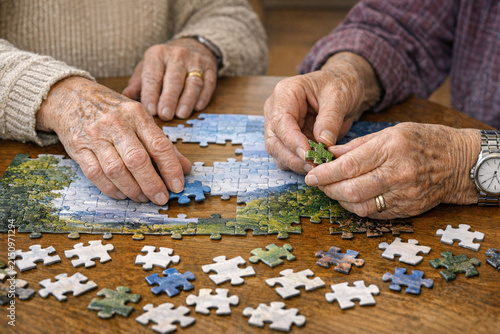 Two older individuals, possibly a couple, focused on completing a puzzle. They are holding and placing puzzle pieces together, engaged in friendly competition or cooperative play.