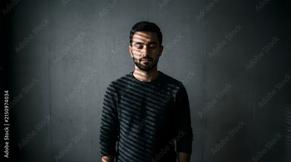 Obraz premium Portrait of a bearded man with closed eyes standing in shadows and light