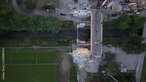 Top-down aerial view of a railway construction site where a new bridge is being built over a small river, with the existing rail line temporarily interrupted by construction.