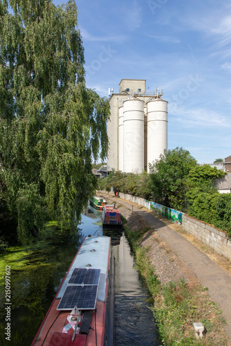 Narrow boats on the River Stort, a canalised river with a towpath, near grain silos in Bishops Stortford, Hertfordshire, England