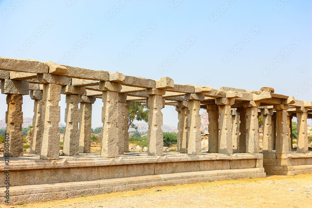Fototapeta premium Ancient stone temple ruins and historic carved architecture in Hampi, India. Beautiful landscape with archaeological site, cultural heritage landmark and popular international tourist destination.