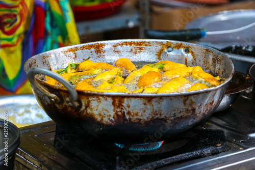 Deep frying traditional Indian street food snacks, mirchi bhajiya or chilli pakora, in hot oil in a pan at a local market stall in Hampi, India. Popular spicy vegetarian snack preparation.
