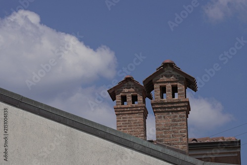 Chimney. A classic red brick chimney with a tiled roof against a blue sky and white clouds.