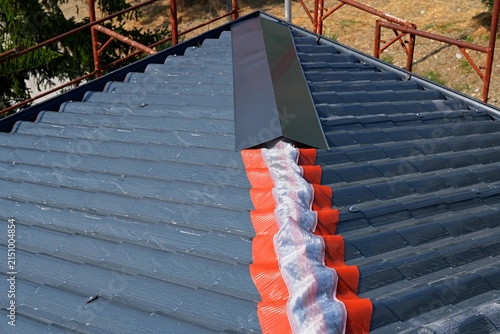 Installing a roof ridge with ventilation tape and a metal ridge cap on a modern tile roof.