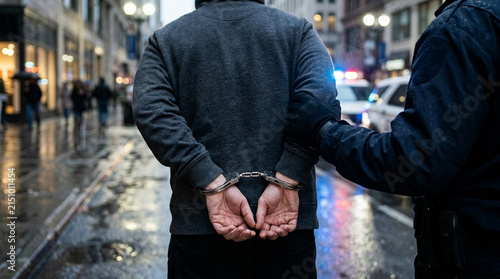 Police Officer Arresting Suspect in Handcuffs on Rainy City Street