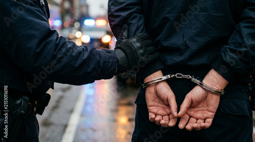 Police officer arresting suspect in handcuffs on wet street with lights
